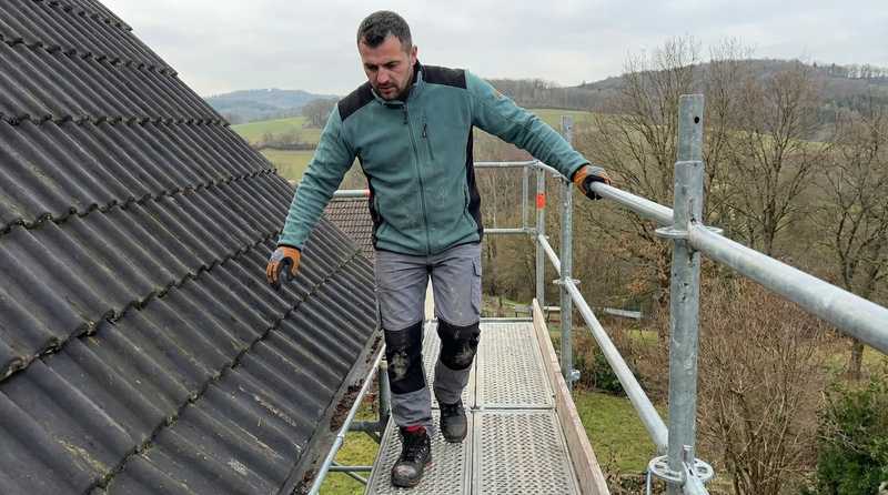 Arbeitssicherheit auf dem Dach - Dachdecker mit PSA und Absturzsicherung auf Steildach